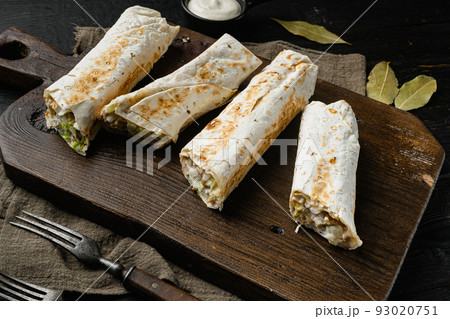 Eastern traditional shawarma with chicken and vegetables, on cutting board, on black wooden table background 93020751