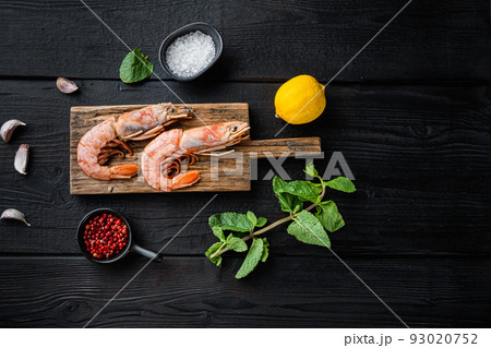 Jumbo shrimps on wooden board with herbs on black wooden background, flat lay with copy space Jumbo shrimps on wooden board with herbs on black wooden background, flat lay with copy space 93020752