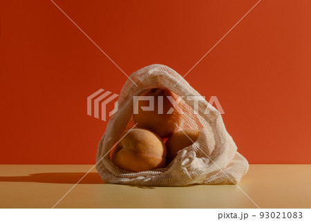 Peaches in a reusable cotton string bag on bright background 93021083