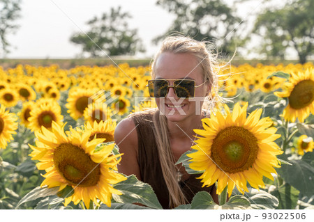 Beautiful woman in sunflower field at sunset enjoying summer nature. Attractive blonde with long healthy hair. 93022506