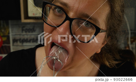 Close-up of the girl with glasses with her tongue licking the cream cheese cream from the whisk. The baker's concept. Cooking a cake in the home kitchen. 93022666