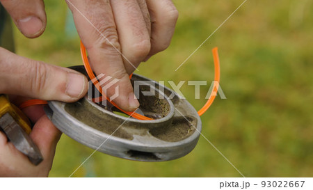 Close-up of a man's hands changing the line on the trimmer reel. Installing a new orange line in the spool of a gasoline trimmer to cut the grass. 93022667