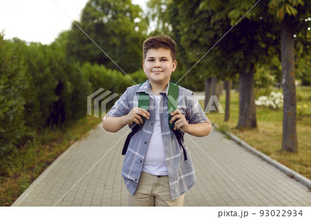 Cheerful Caucasian boy teenager with school backpack on back walks after study day in summer park 93022934