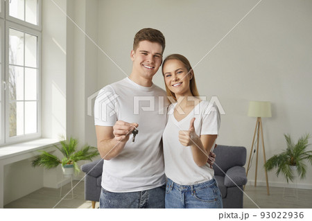 Happy young couple showing the key to their new house, smiling and giving a thumbs up 93022936