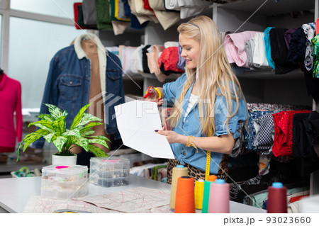 A seamstress cuts a paper mold from the garment she is designing. 93023660