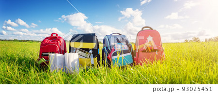 Children's schoolbags of different colours standing on the green field 93025451
