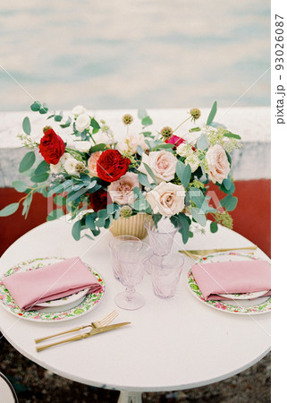Bouquet of flowers in a vase stands on a table near plates and glasses Bouquet of flowers in a vase stands on a table near plates and glasses 93026087