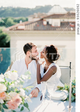 Bride and groom are sitting at the table on the roof of the building 93026092