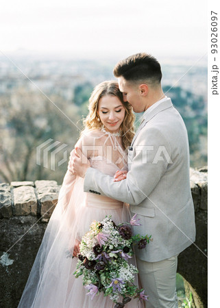 Groom hugs bride with a bouquet on the roof of the house. Bergamo, Italy 93026097