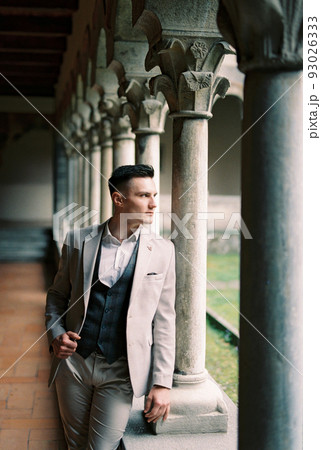 Man in a suit stands near a column on the terrace and looks out into the garden. Como, Italy 93026333