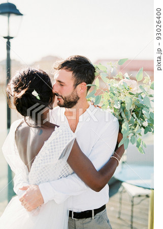 Groom hugs bride with a bouquet of flowers on the roof of the building 93026400