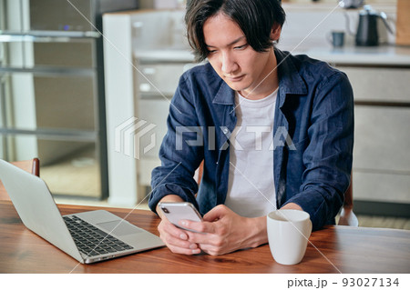 テレワーク中にスマホを操作する若い男性 93027134