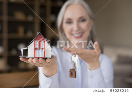 Happy mature mortgage broker woman holding keys and small model 93028016