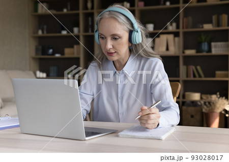 Senior mature student woman in big headphones watching learning webinar 93028017