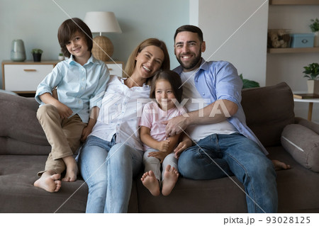 Happy couple with children posing for camera seated on couch 93028125