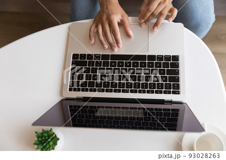 Young woman using laptop, sitting at coffee table, typing 93028263