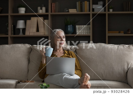 Happy dreamy pensive retired woman relaxing on comfortable sofa Happy dreamy pensive retired woman relaxing on comfortable sofa 93028426