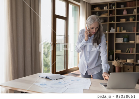 Serious elderly business leader woman standing at paper marketing reports 93028661