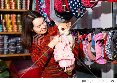 Positive woman holding dog and choosing clothes in petshop 93031139