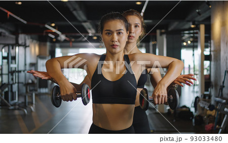 Sporty girl doing weight exercises with the help of her personal trainer at the gym. Sporty girl doing weight exercises with the help of her personal trainer at the gym. 93033480