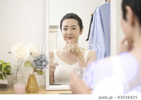 ビューティ　鏡の前で薬を飲むショートヘアのミドル女性 93036925