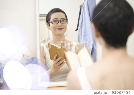 鏡の前でめがねを掛けて本を読むショートヘアのミドル女性 93037454