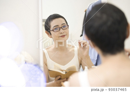 鏡の前でめがねを掛けて本を読むショートヘアのミドル女性 93037465