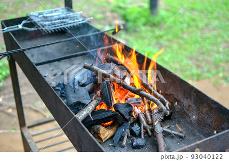 an empty brazier with a burning bonfire fire against the background of green grass preparing for a barbecue. an empty brazier with a burning bonfire fire against the background of green grass preparing for a barbecue. 93040122