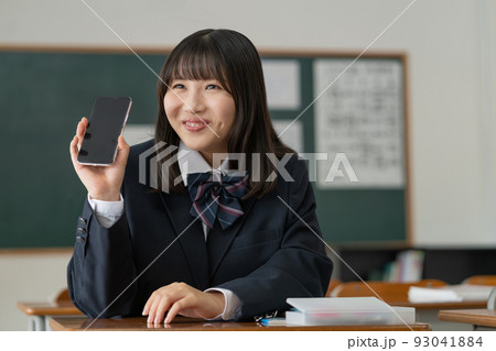 学校の教室で休み時間にスマホを手に友達と会話する女子高生 学校の教室で休み時間にスマホを手に友達と会話する女子高生 93041884