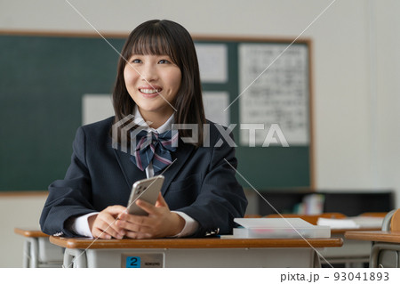 学校の教室で休み時間にスマホを手に友達と会話する女子高生 93041893