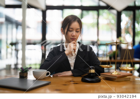Thinking woman lawyers discussing contract papers with brass scale in office. Law, legal services, advice, Justice and real estate concept. Thinking woman lawyers discussing contract papers with brass scale in office. Law, legal services, advice, Justice and real estate concept. 93042194