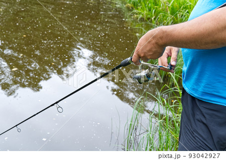 fisherman hand with spinning and reel on the summer lake, close-up. fisherman hand with spinning and reel on the summer lake, close-up. 93042927