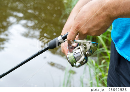 fisherman hand with spinning and reel on the summer lake, close-up. fisherman hand with spinning and reel on the summer lake, close-up. 93042928