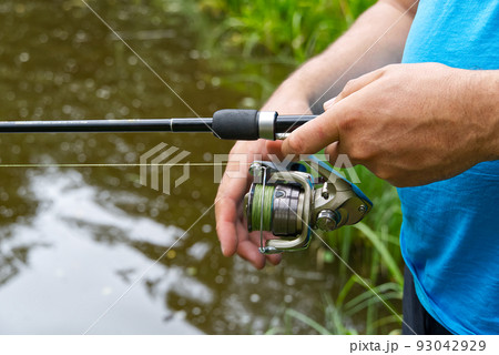 fisherman hand with spinning and reel on the summer lake, close-up. fisherman hand with spinning and reel on the summer lake, close-up. 93042929