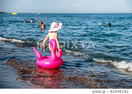 Small child with inflatable pink flamingo walking into the sea Small child with inflatable pink flamingo walking into the sea 93046282