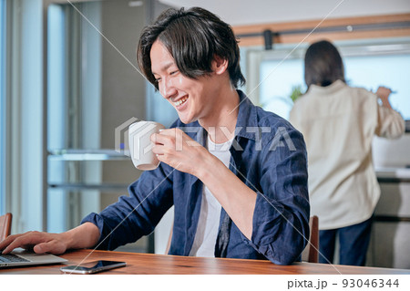 テレワーク中にコーヒーを飲む男性と家事をする女性 93046344
