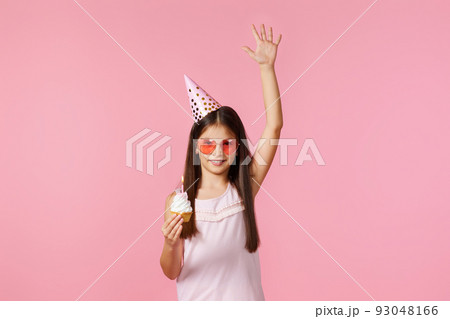 happy little birthday girl with party cone holding cupcake 93048166