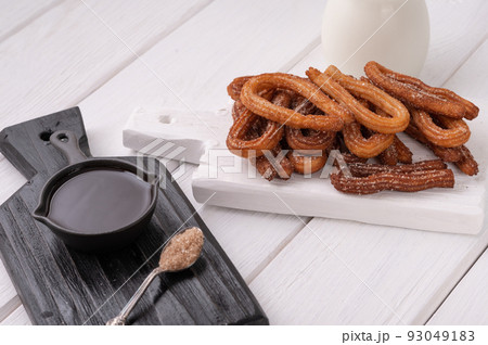 Homemade churros with chocolate on a white wooden background. 93049183