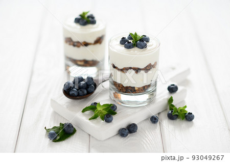 Dessert with cottage cheese, fresh blueberries and granola in a glass on a white wooden background. Dessert with cottage cheese, fresh blueberries and granola in a glass on a white wooden background. 93049267