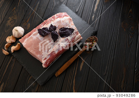 A large piece of pork loin with basil on a rustic dark background. 93049286