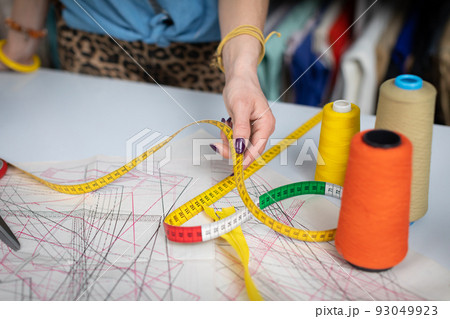 Colorful threads on bobbins stand on a sewing table. Tailor's patterns. Colorful threads on bobbins stand on a sewing table. Tailor's patterns. 93049923