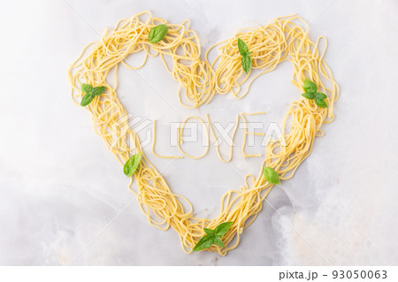 Decorative heart shaped pasta still life formed of pasta topped with tomatoes, basil 93050063