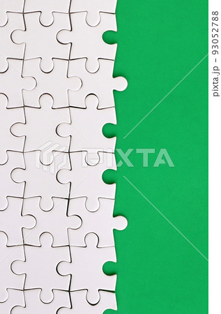 Fragment of a folded white jigsaw puzzle on the background of a green plastic surface. Texture photo with copy space for text Fragment of a folded white jigsaw puzzle on the background of a green plastic surface. Texture photo with copy space for text 93052788