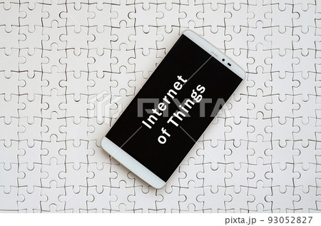 A modern big smartphone with a touch screen lies on a white jigsaw puzzle in an assembled state with inscription. Internet of things A modern big smartphone with a touch screen lies on a white jigsaw puzzle in an assembled state with inscription. Internet of things 93052827