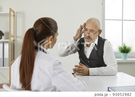 Older man during visit or consultation at clinic tells doctor about his severe headaches. Older man during visit or consultation at clinic tells doctor about his severe headaches. 93052982