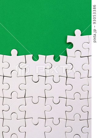 Fragment of a folded white jigsaw puzzle on the background of a green plastic surface. Texture photo with copy space for text 93053386
