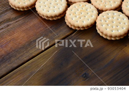 A round sandwich cookie with coconut filling lies in large quantities on a brown wooden surface. Photo of edible treats on a wooden background with copy space 93053404