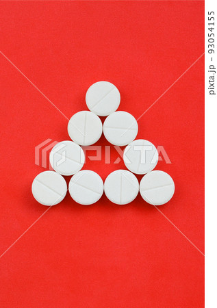 Several white tablets lie on a bright red background in the form of an even triangle. Background image on medicine and pharmaceutical topics Several white tablets lie on a bright red background in the form of an even triangle. Background image on medicine and pharmaceutical topics 93054155