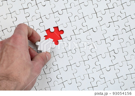 The texture of a white puzzle puzzle in the assembled state with one missing element that the male hand puts in 93054156