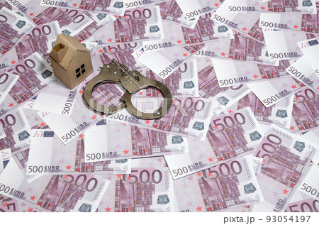 Scam with real estate. Cheating when buying or renting a house. Punishment for deception. A toy house with handcuffs on a many 500 purple euro banknotes 93054197